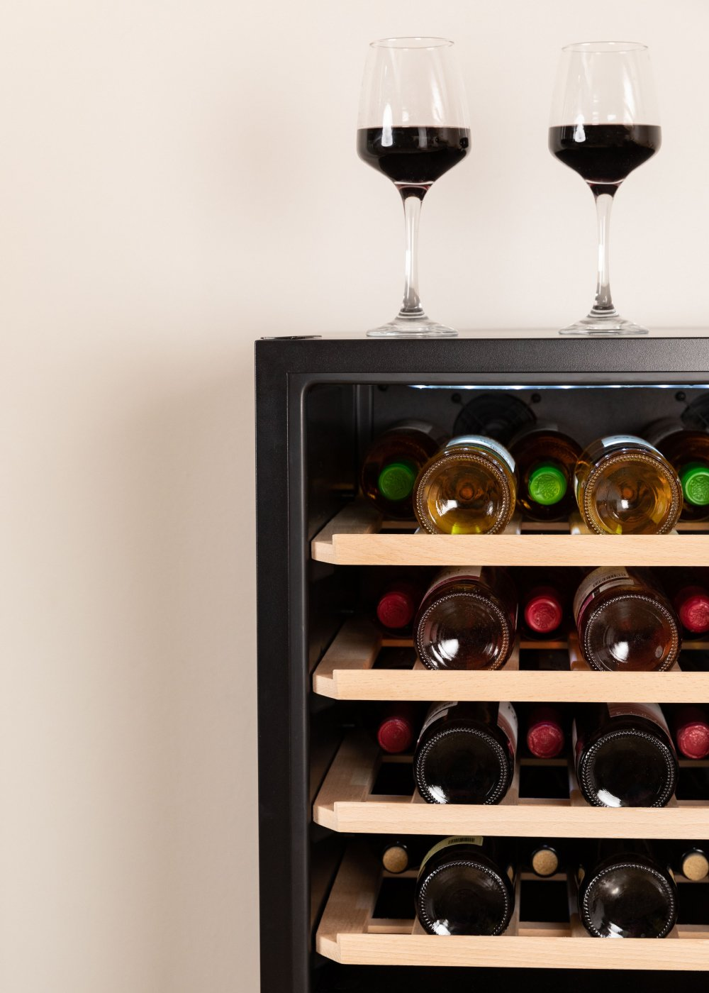 Botellas de vino en una vinoteca. Dos copas de vino tinto encima. Botellas visibles a través de la puerta de cristal.
