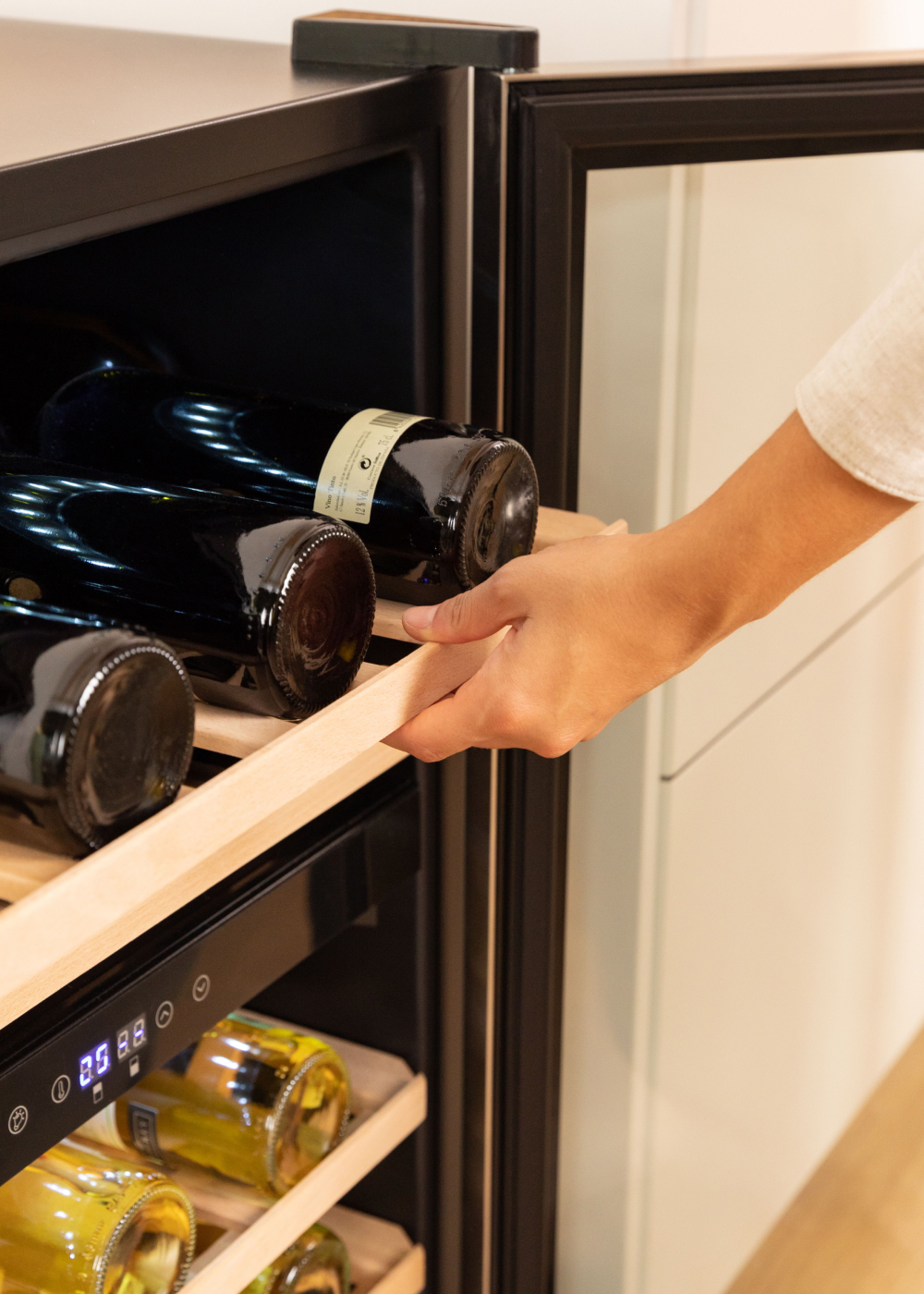 Una mano saca un estante de madera de una vinoteca llena de botellas de vino.