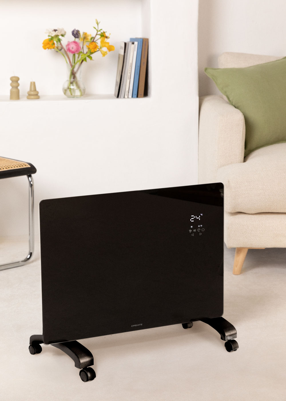 Calentador eléctrico negro con ruedas. Tiene una pantalla digital que muestra 24. Flores y sofá en el fondo.