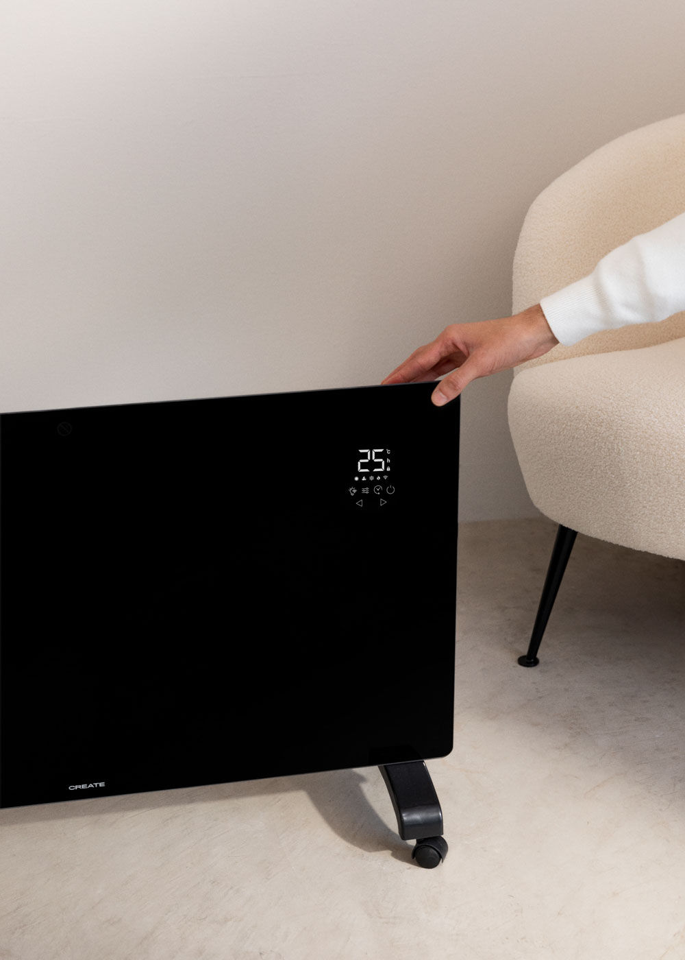 Un calentador negro muestra una pantalla digital. Una mano lo ajusta. Un sillón está cerca.