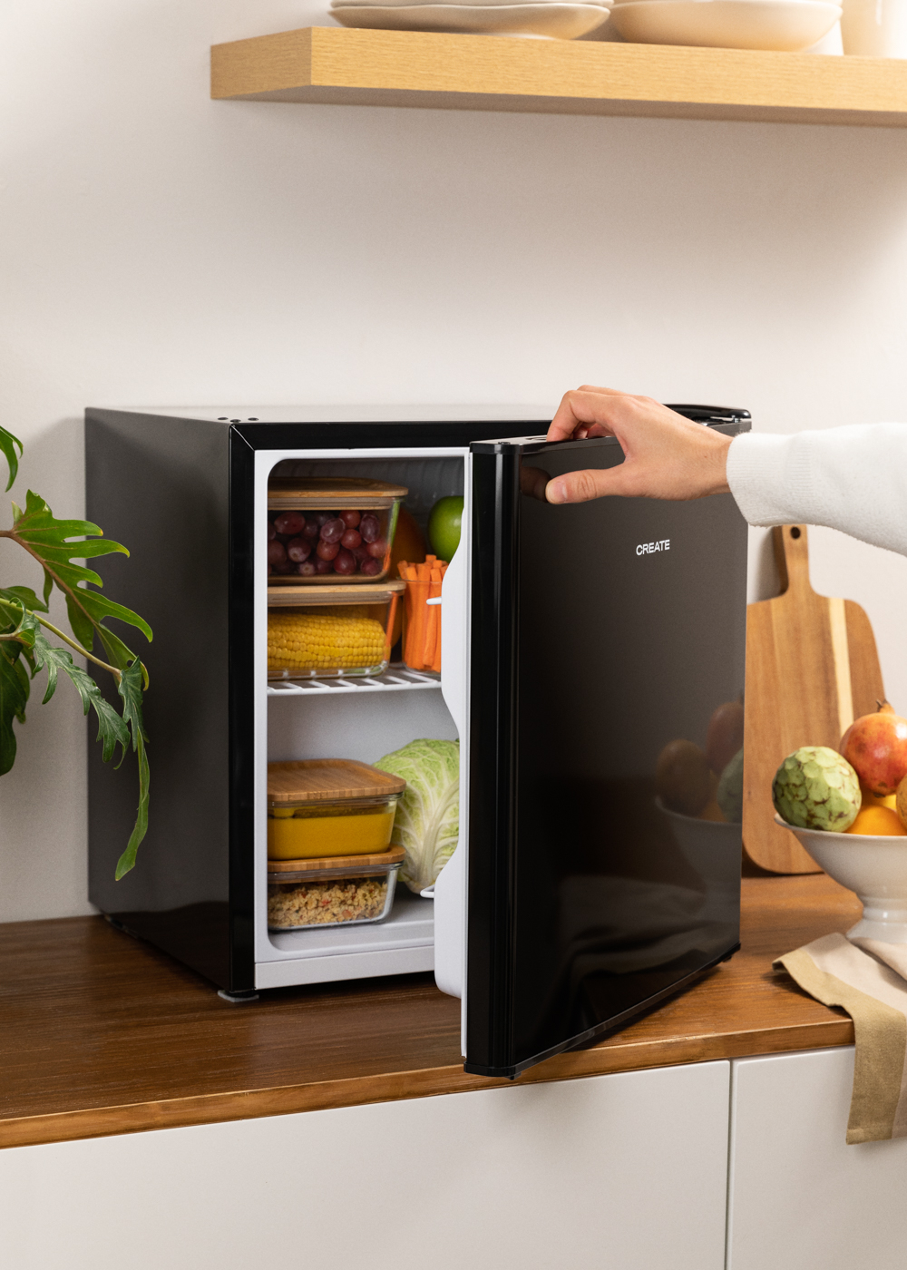 Mini nevera negra con puerta abierta. Alimentos visibles dentro. Mano alcanzando la puerta.