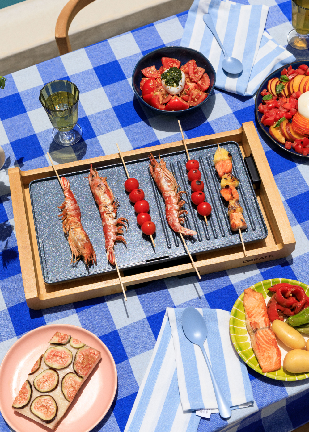 Escena al aire libre con comida en una mesa. Comida a la parrilla y frutas en mantel a cuadros azul y blanco.