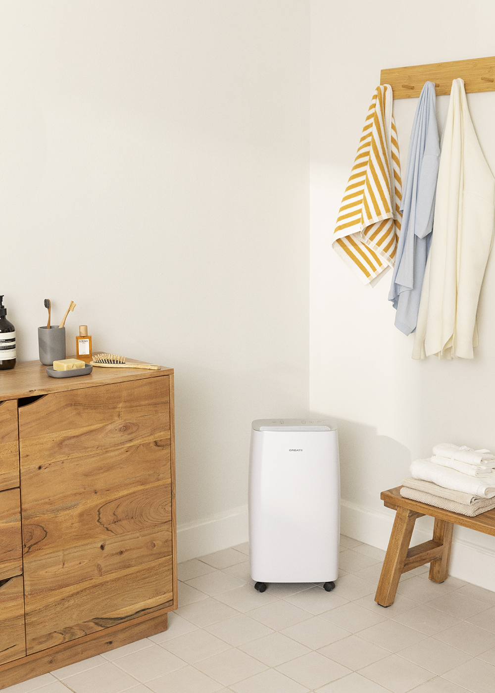 Un baño con un mueble de madera y un purificador de aire blanco. Toallas colgadas al fondo.