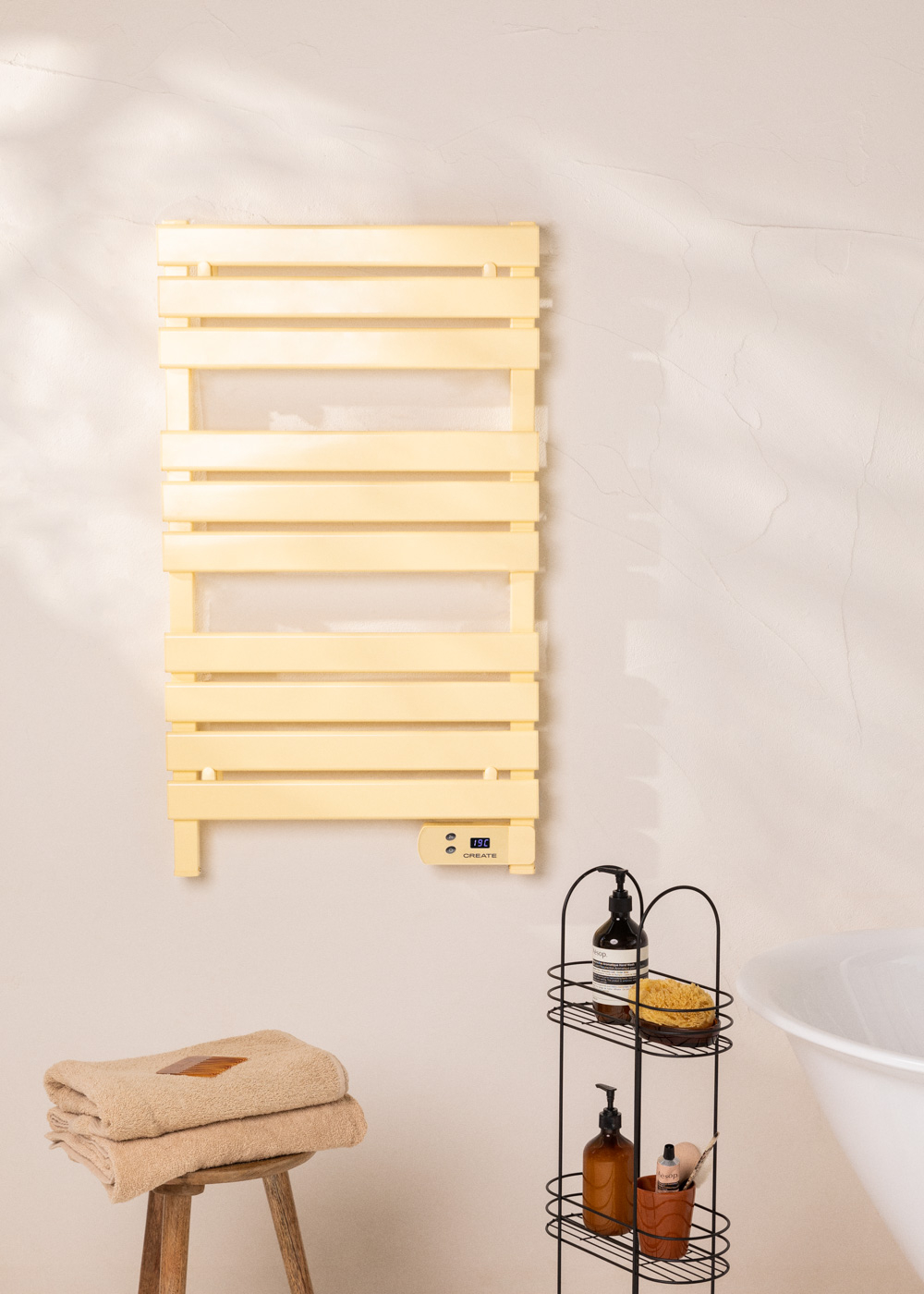 Calentador de toallas amarillo, montado en la pared. Toallas en un taburete de madera debajo. Estante baño a la derecha.