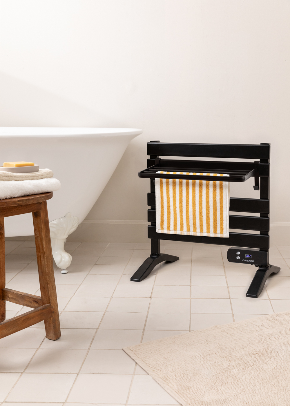 Un calentador de toallas negro con una toalla a rayas en un baño. Una bañera y un taburete están cerca.