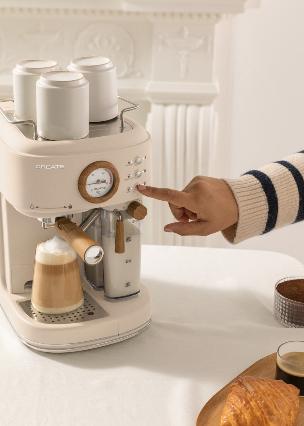 Persona presionando un botón en una máquina de espresso crema. Café y croissant en la mesa.