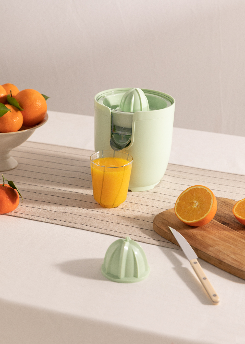 Exprimidor con naranjas, jugo y tabla de cortar. Naranjas en un bol y sobre una mesa.