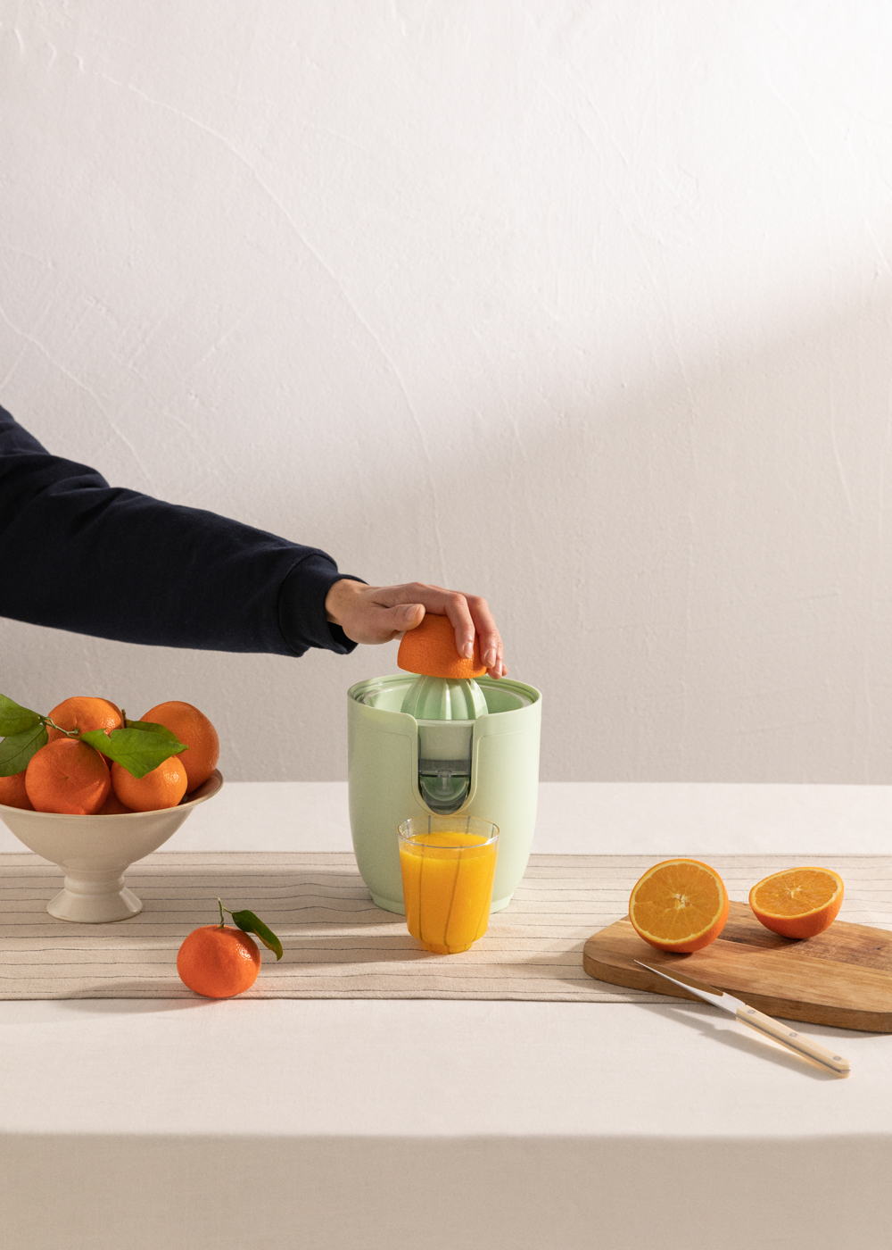 Persona exprimiendo naranja en vaso con exprimidor. Naranjas en la mesa. Fondo blanco.
