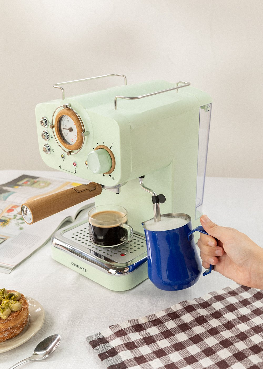 Máquina de espresso verde menta con taza de café. Jarra azul para espumar leche y otros elementos.