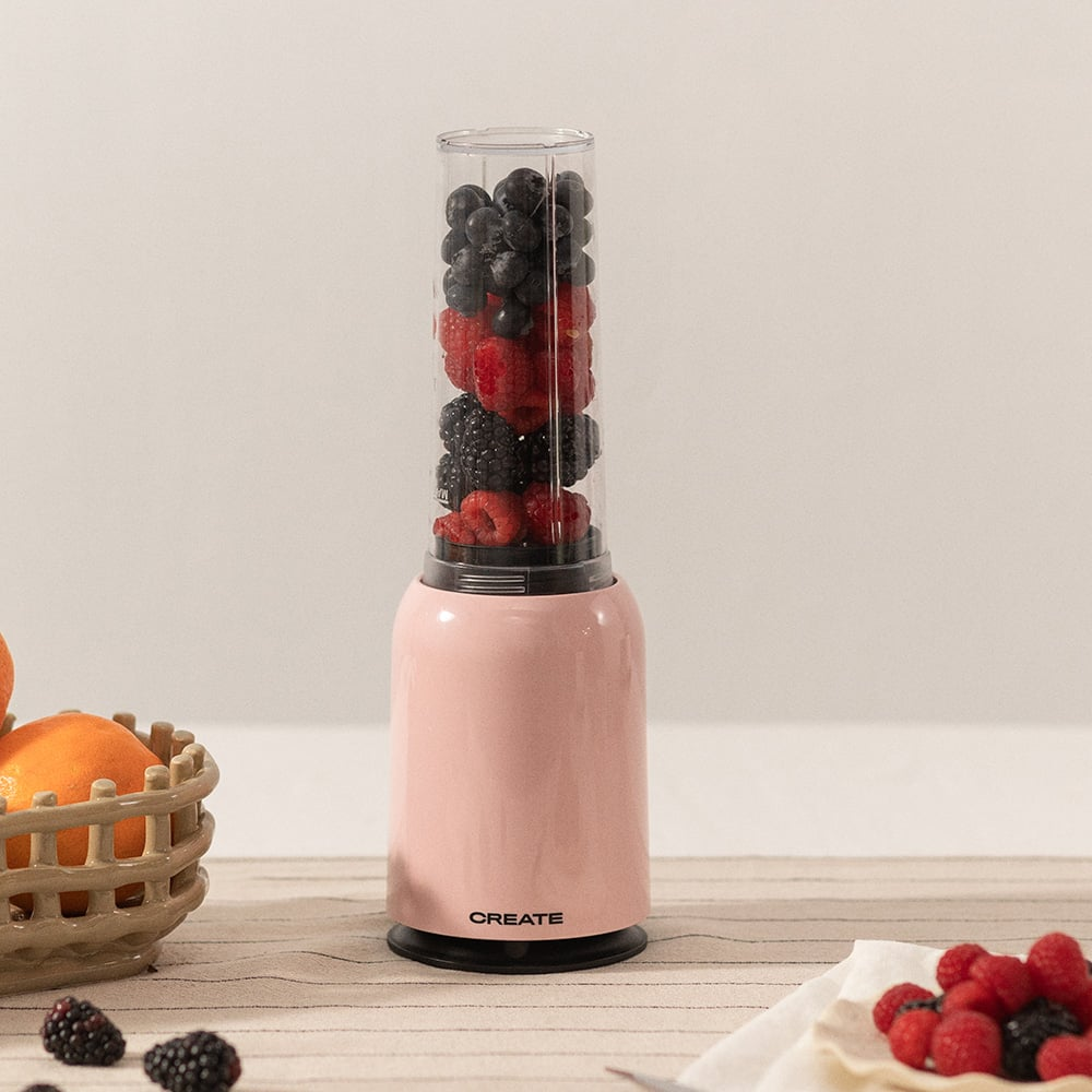 Licuadora rosa con bayas y un cuenco de fruta al lado.