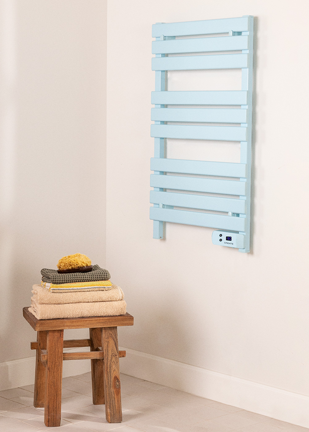 Calentador de toallas azul en pared blanca con toallas en taburete de madera.