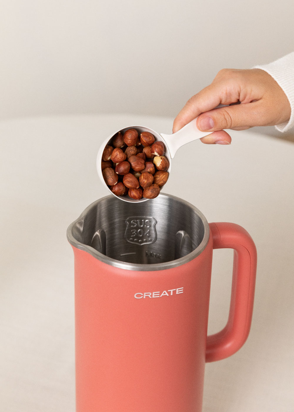 Una mano vierte avellanas de una taza blanca en una licuadora roja.