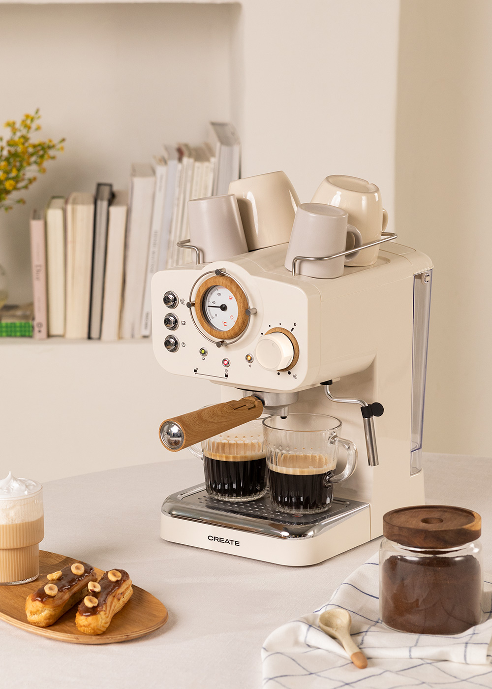 Máquina de café con dos tazas, algunas tazas arriba y pasteles al lado.