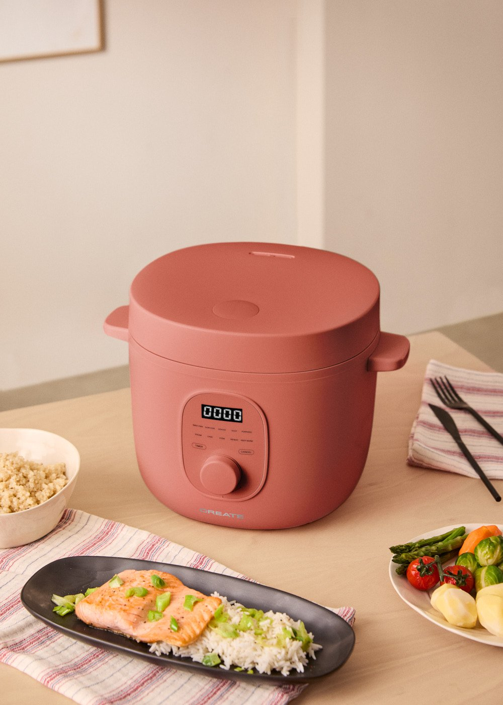 Olla de cocción lenta rosa con texto CREATE y platos de comida en una mesa de madera.