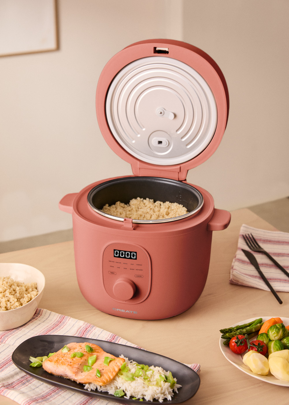 Vaporera rosa con tapa abierta, arroz en la olla y plato con salmón y verduras.