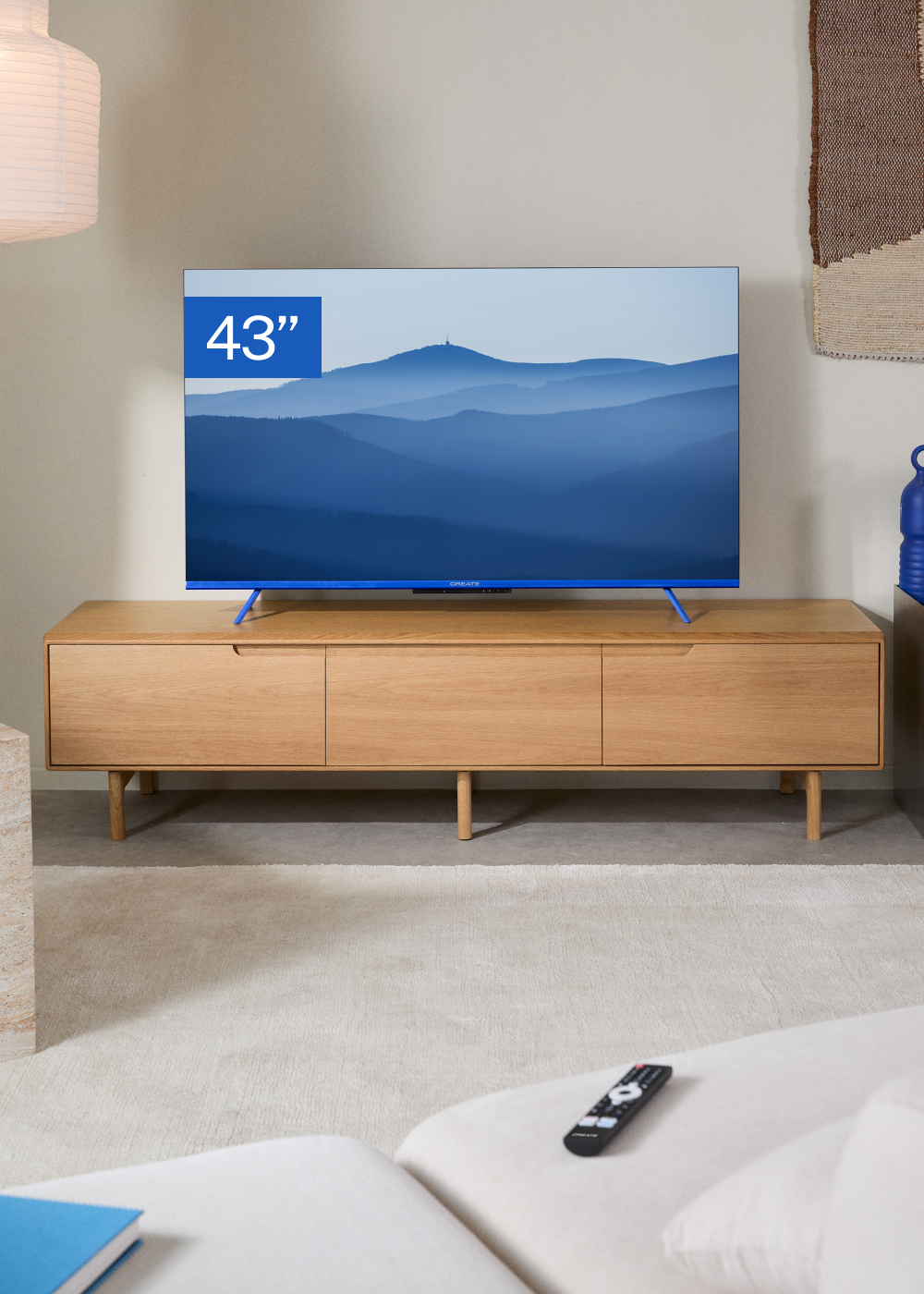 Un televisor de 43 pulgadas sobre un mueble de madera. Mando a distancia en primer plano, paisaje montañoso en pantalla.