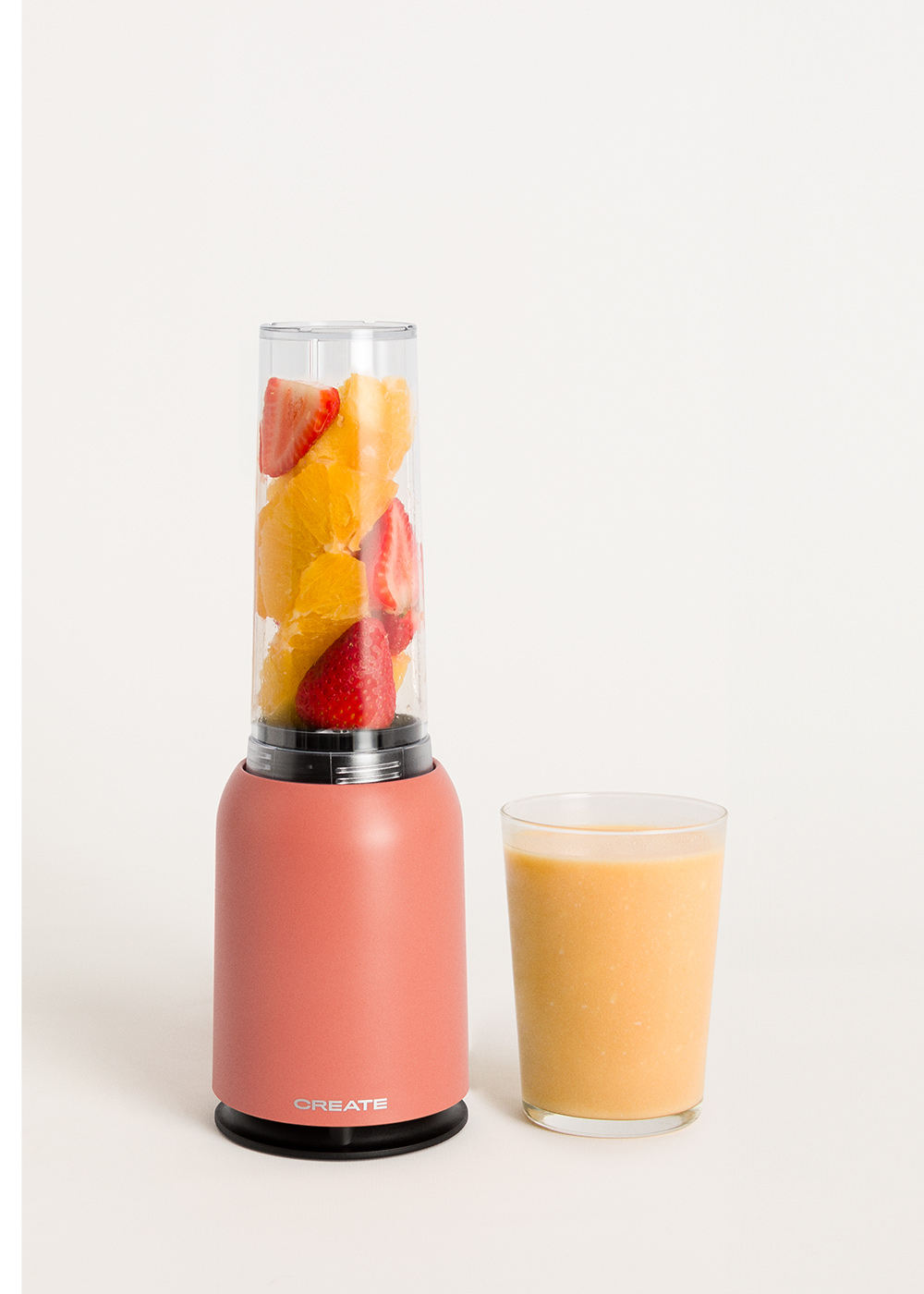 Una licuadora roja con naranjas y fresas dentro, y un vaso de batido.
