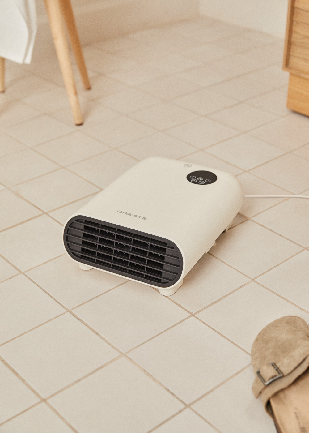 Un calefactor eléctrico blanco sobre un suelo de baldosas. Un par de zapatillas en primer plano.