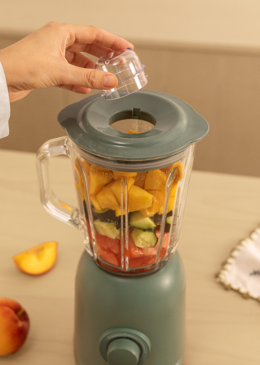 Eine Person, die Zutaten in einen Mixer mit Früchten darin gießt.