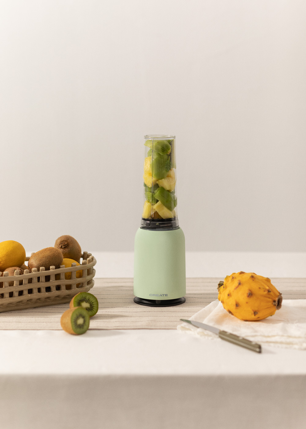 Una licuadora con frutas dentro, kiwi, limón y una fruta del dragón en la mesa.