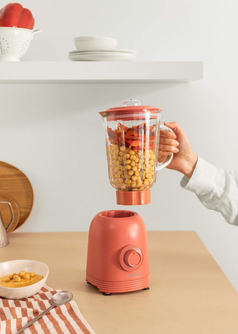 Hand hält Mixerbehälter mit Kichererbsen und Paprika. Basis ist abgenommen.