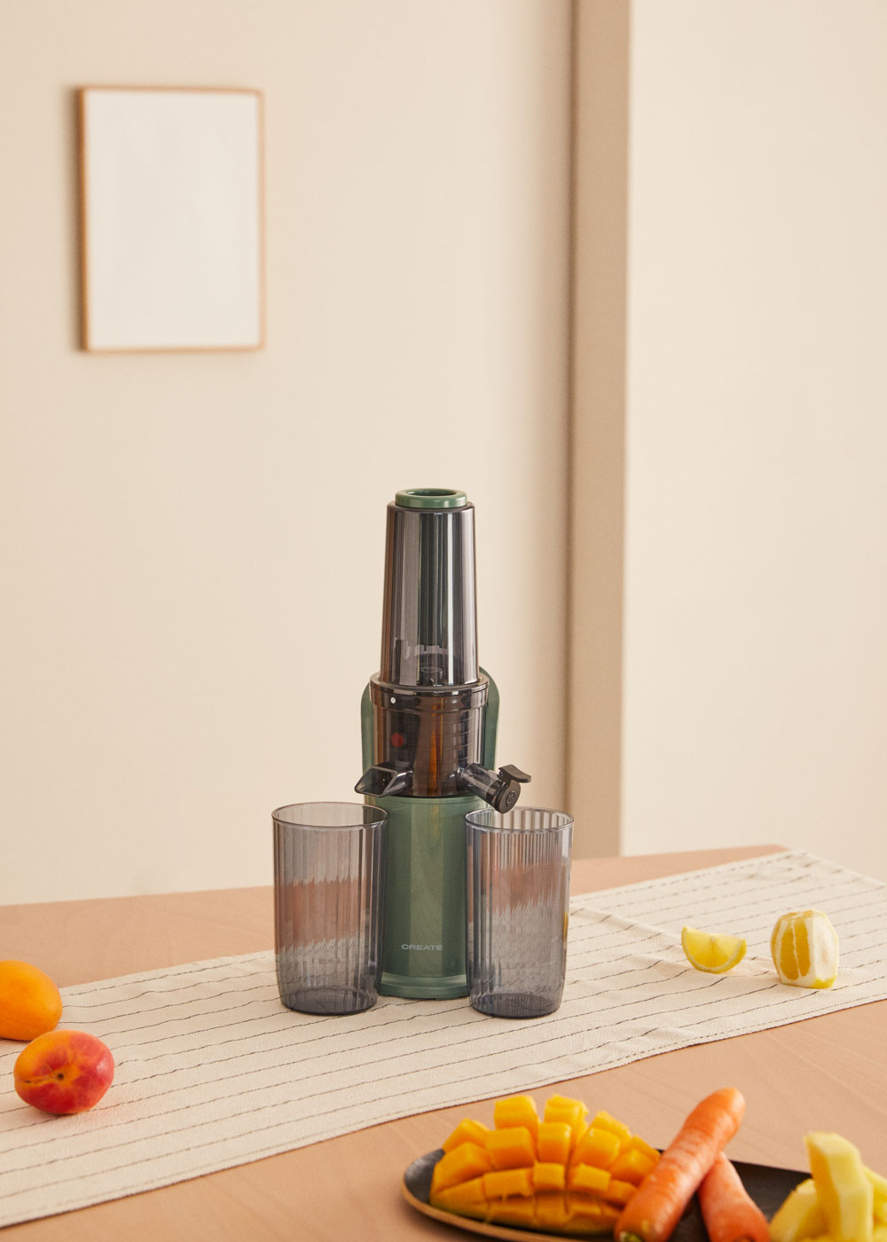 Exprimidor con dos vasos, frutas y una mesa de madera. Una mano de mujer está sobre la mesa.