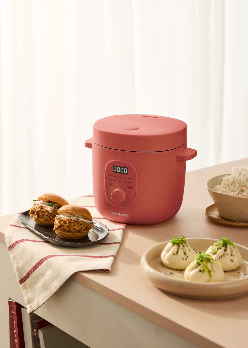 Una olla de cocción lenta rosa con comida en la mesa. Sándwiches y empanadillas en primer plano.