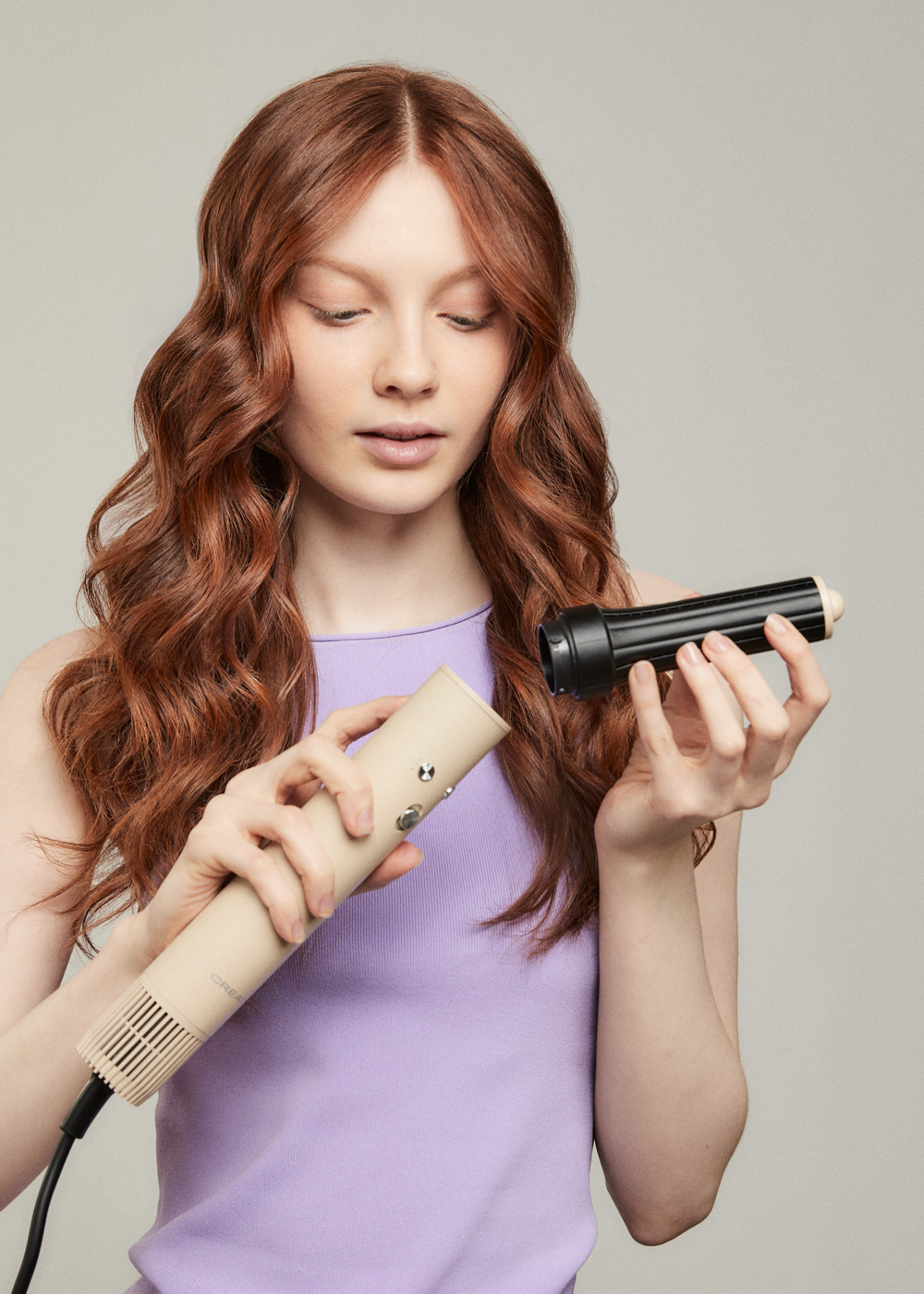 Mujer pelirroja sosteniendo una herramienta para el cabello beige con accesorios negros.