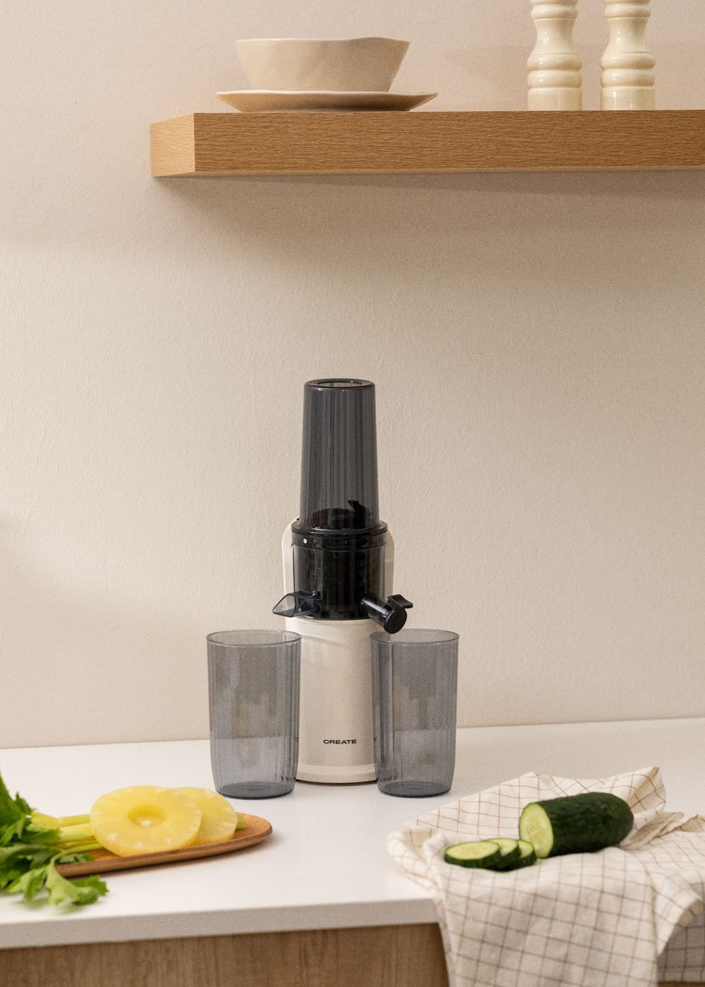 Exprimidor con vasos e ingredientes como piña y pepino sobre encimera blanca.
