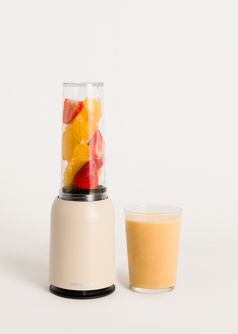 Ein Mixer mit Orangen- und Erdbeerscheiben und ein Glas Orangensmoothie auf weißem Hintergrund.