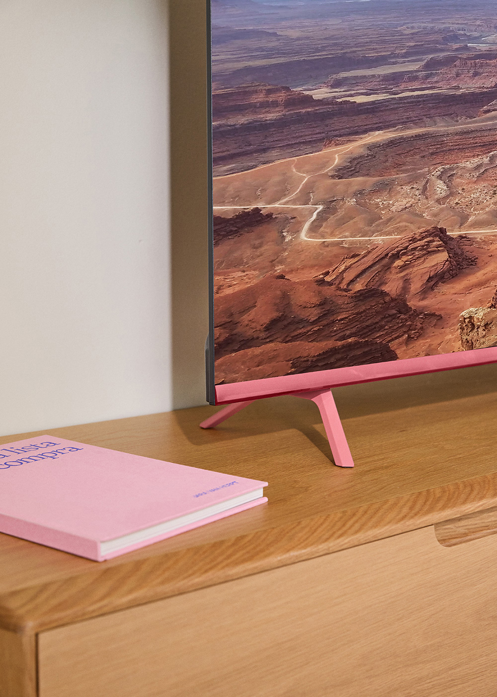 Un televisor rosa sobre un mueble de madera con un libro rosa. Un paisaje montañoso se muestra en la pantalla.