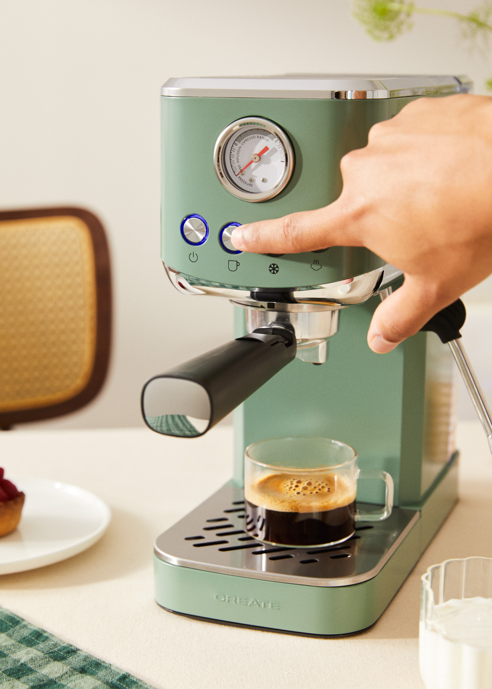 Máquina de espresso verde con una mano presionando un botón. Una taza de café debajo.