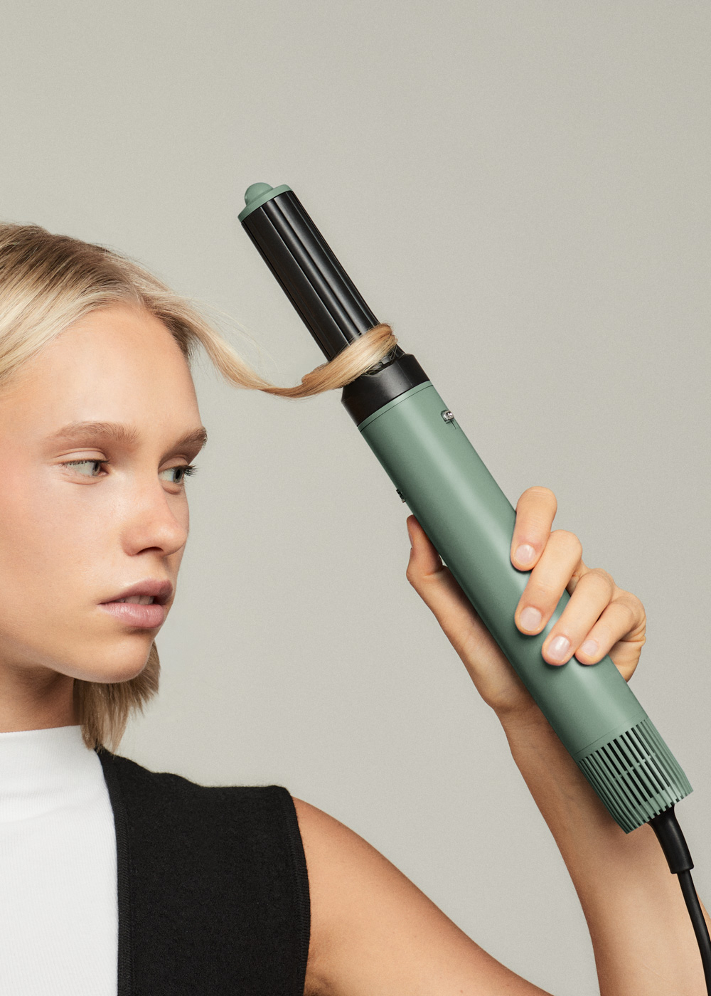 Mujer rizándose el pelo con un rizador verde. Mira hacia la izquierda.