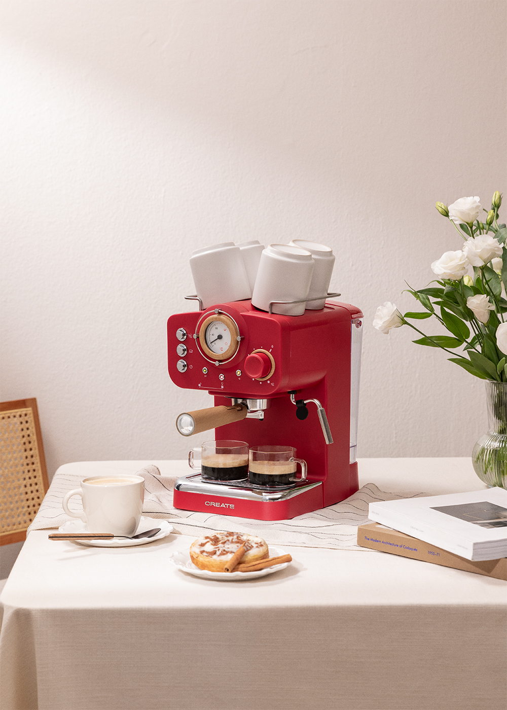 Máquina de espresso roja con dos tazas de café. Tazas arriba, flores y un libro.