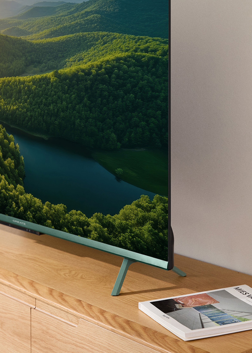 TV verde en soporte de madera, mostrando un paisaje, con una revista en el soporte.