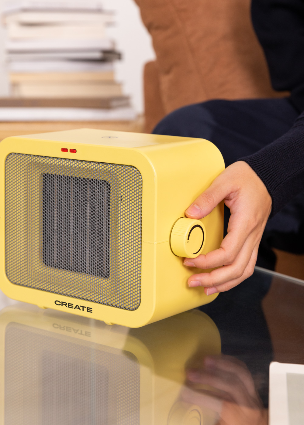 Una persona ajustando un calefactor eléctrico amarillo con rejilla frontal y logo CREATE.