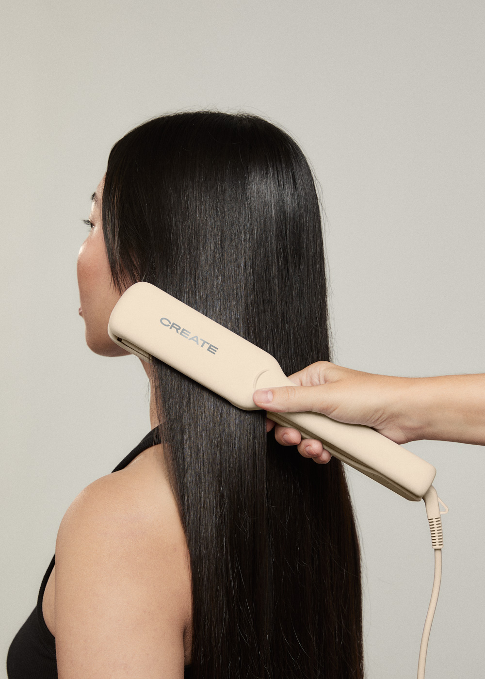 Persona usa una plancha de pelo Create en el pelo largo y negro de otra persona. La mano sostiene la plancha.