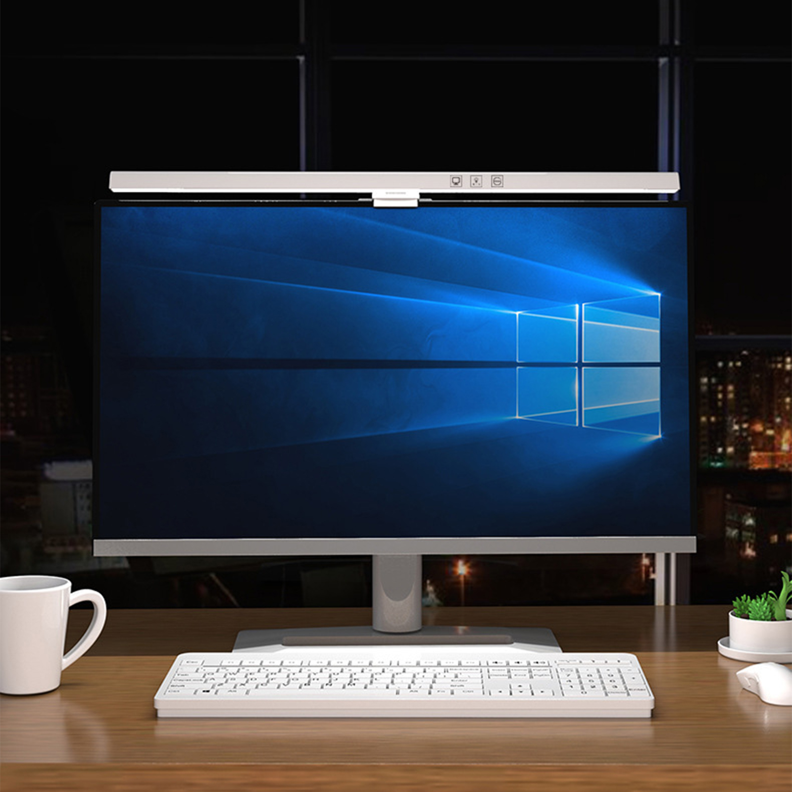Monitor, Tastatur und eine weiße Tasse auf einem Schreibtisch mit Stadtblick im Hintergrund.