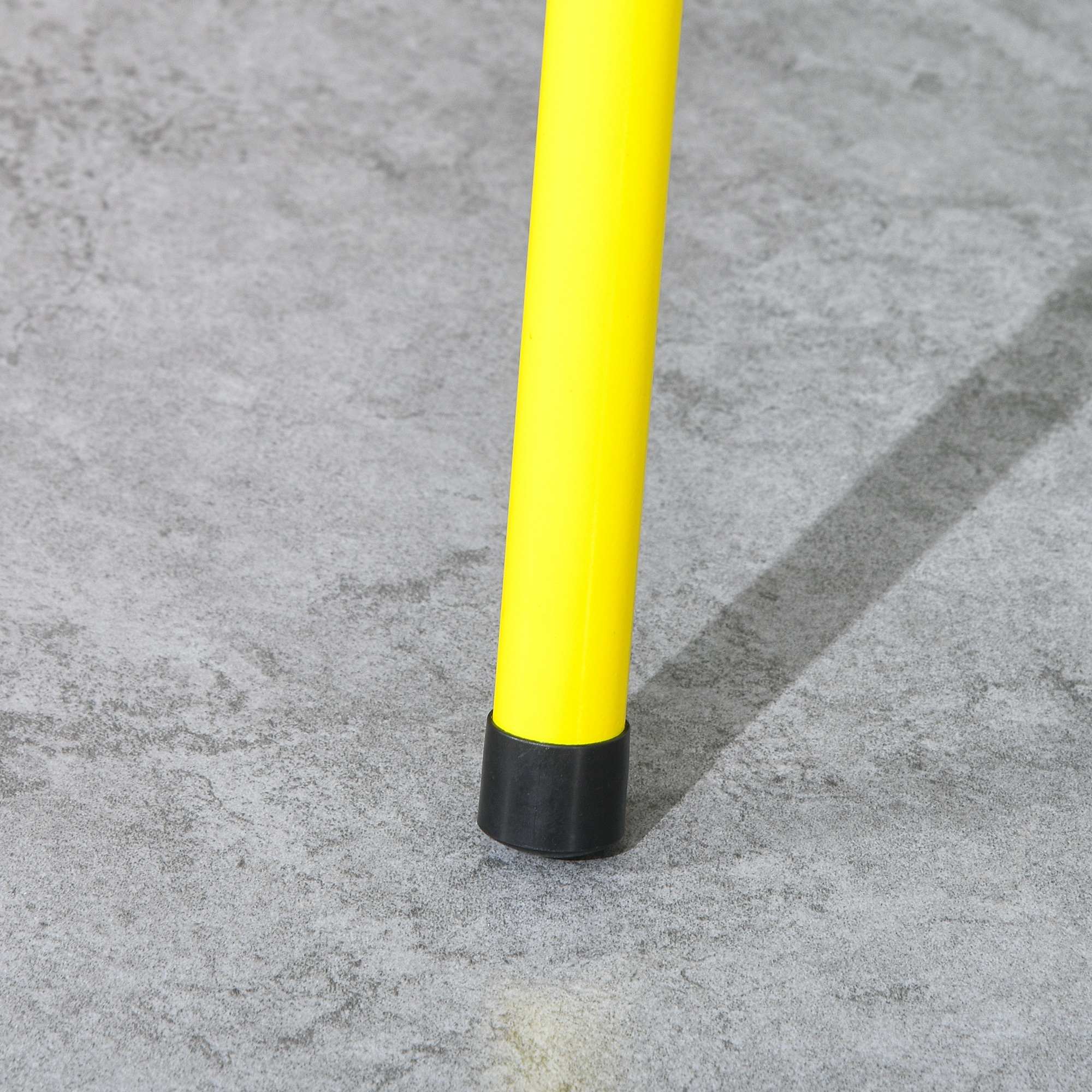 Gelbes Metallbein mit schwarzem Gummifuß auf grauem, betonähnlichem Untergrund.