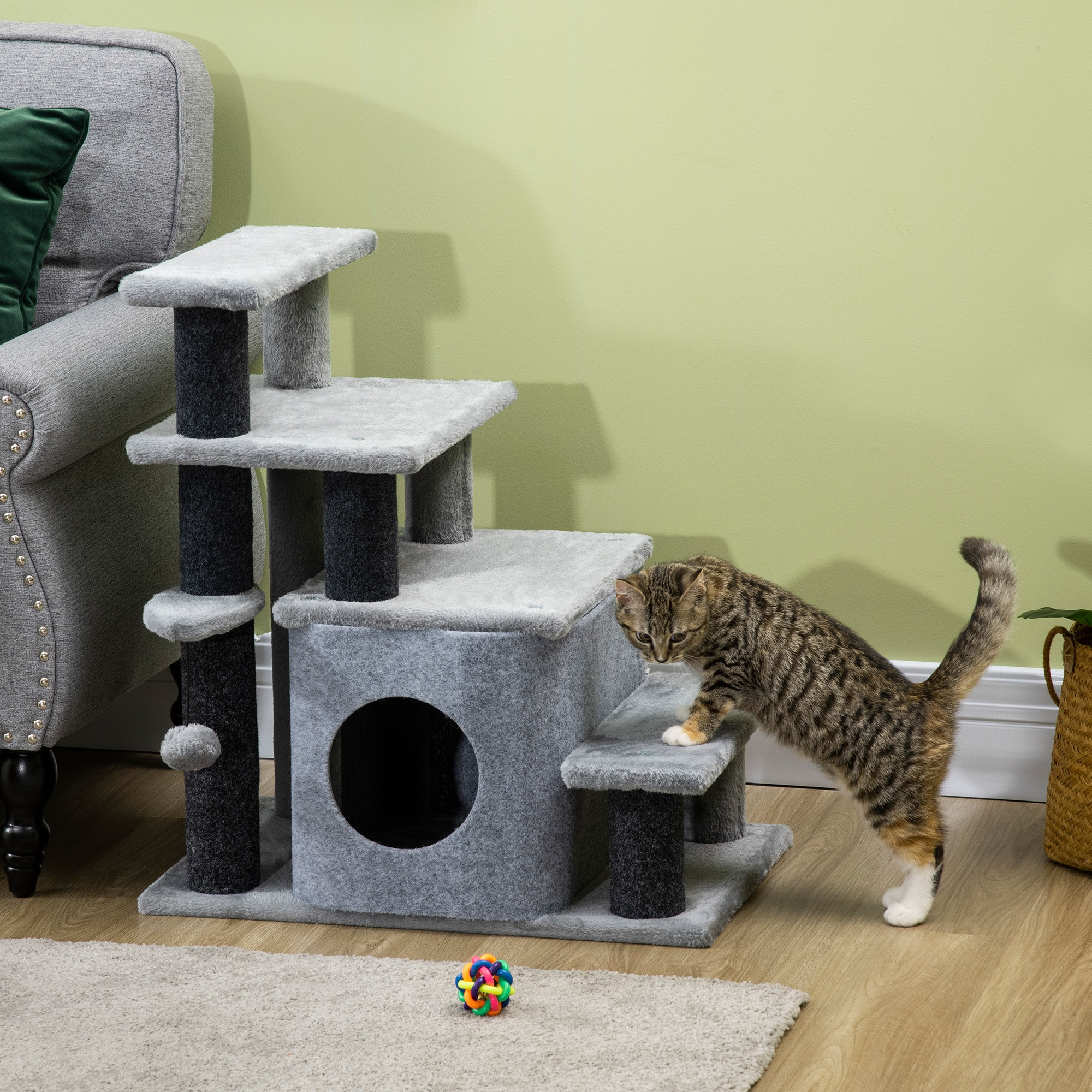 Katze klettert grauen Kratzbaum mit Ebenen und Ball. Grünes Wand im Hintergrund.