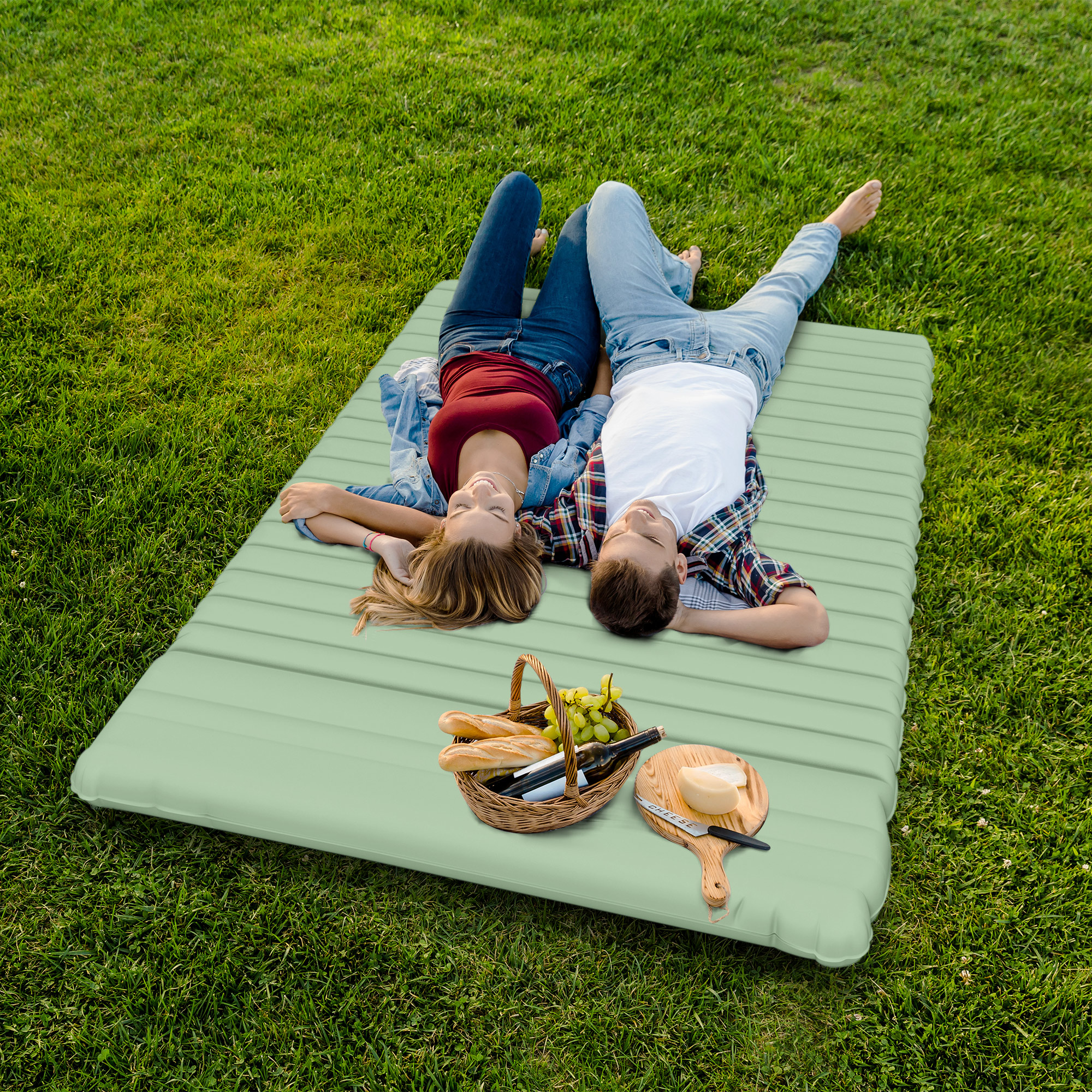 Paar liegt auf einer grünen Matte im Gras. Picknickkorb und Essen sind in der Nähe.