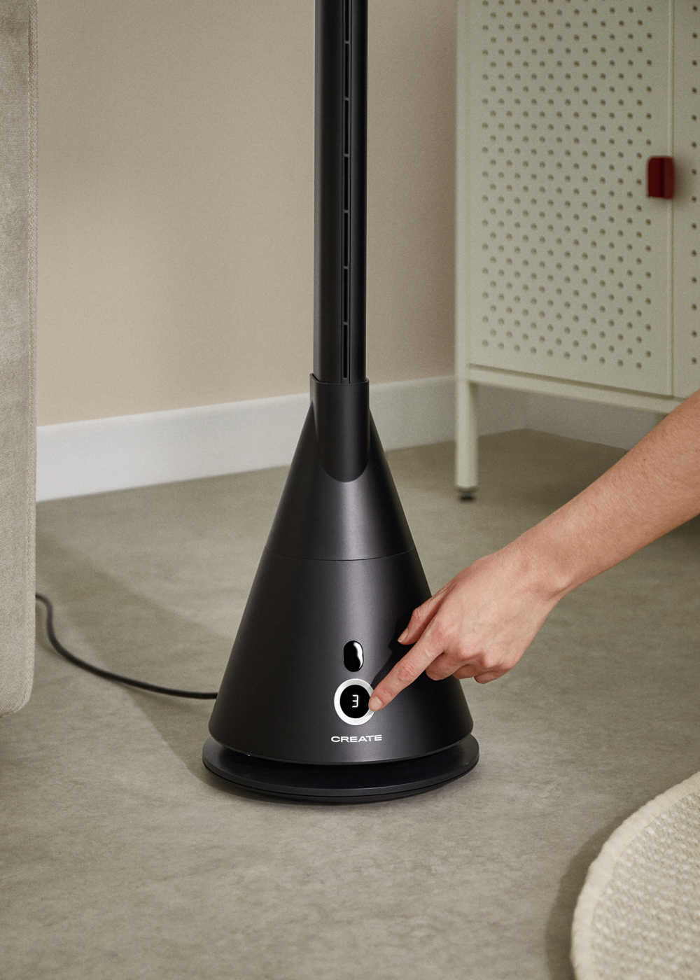 Una mano presiona un botón en un ventilador negro. El ventilador es alto y en forma de cono. La palabra 'CREATE' está en él.
