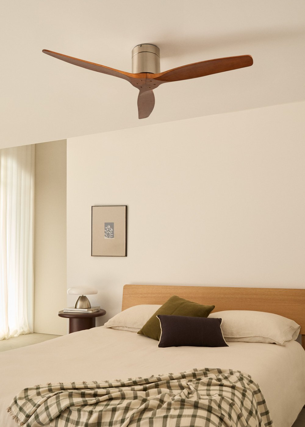 Ventilador de techo con tres aspas de madera. Cama, marco y arte en la escena.