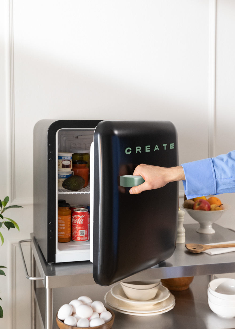 Una mano abriendo un mini refrigerador negro sobre un carrito de acero inoxidable, con comida dentro.