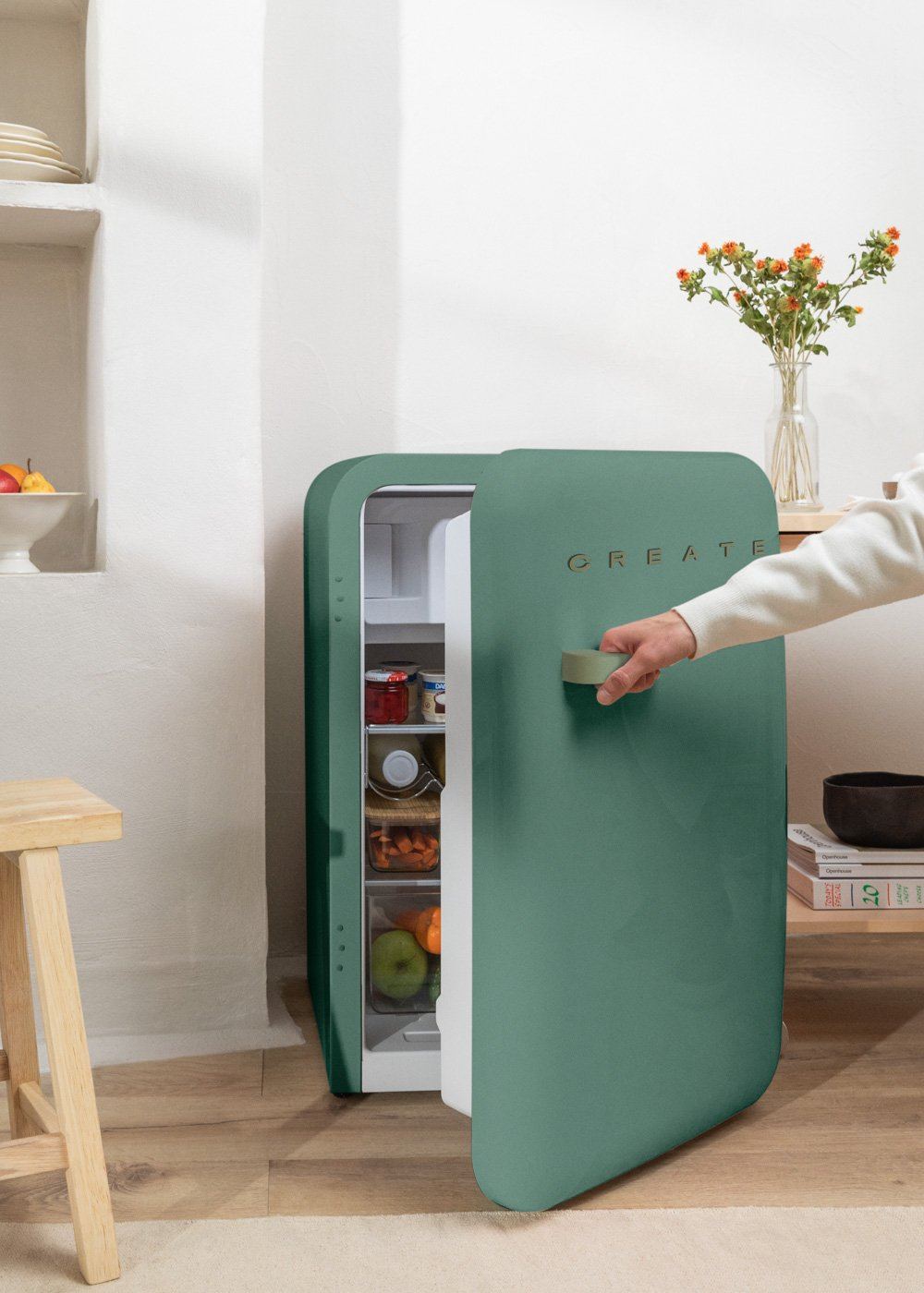 Refrigerador retro verde con puerta abierta. Mano entrando. Taburete de madera al lado.