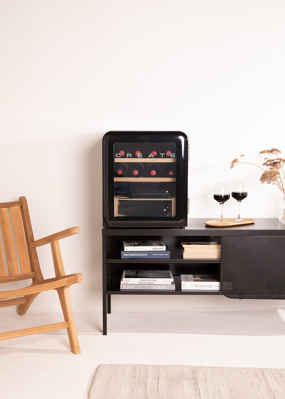 Enfriador de vino negro sobre un mueble negro con copas de vino y una silla de madera. Fondo de pared blanca.