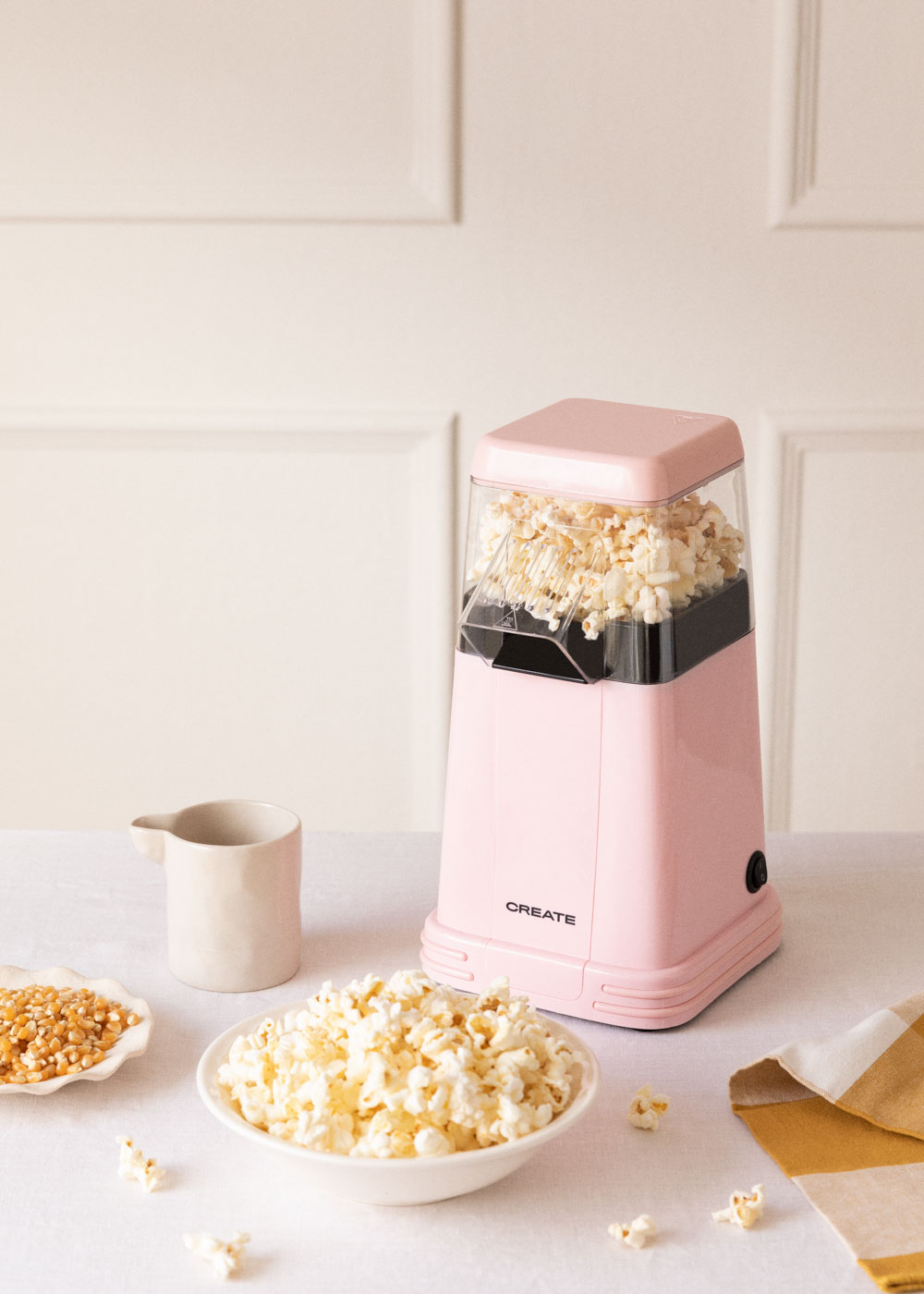 Máquina de palomitas rosa con palomitas en el bol. Un bol con granos y una taza en la mesa.