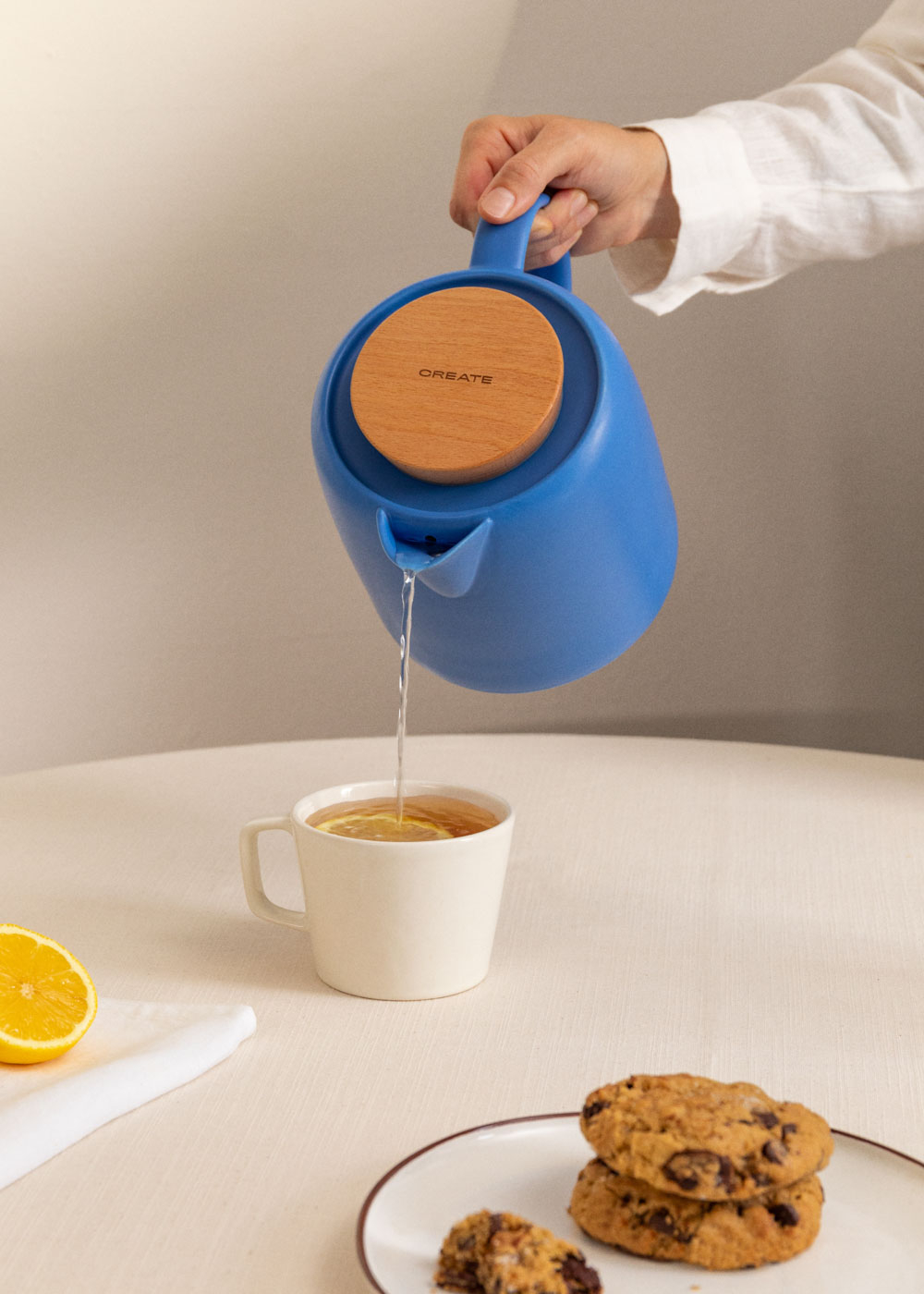 Tetera azul vertiendo agua en una taza con rodajas de limón. Galletas y limón.