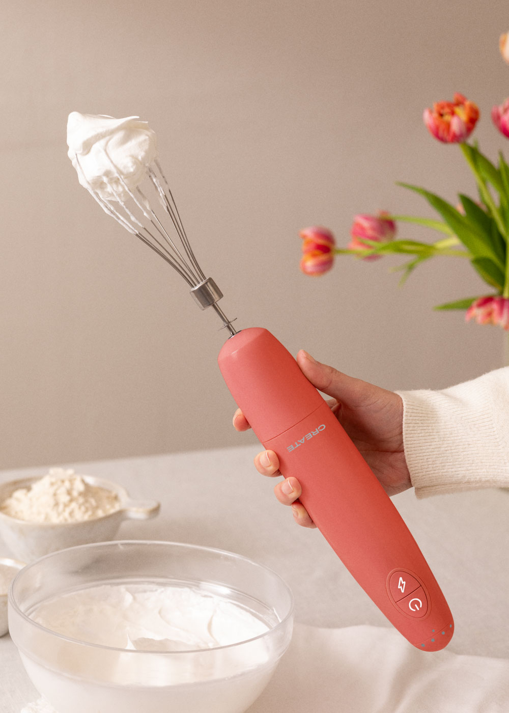 Un batidor eléctrico rosa con crema batida en un cuenco y un ramo de flores.