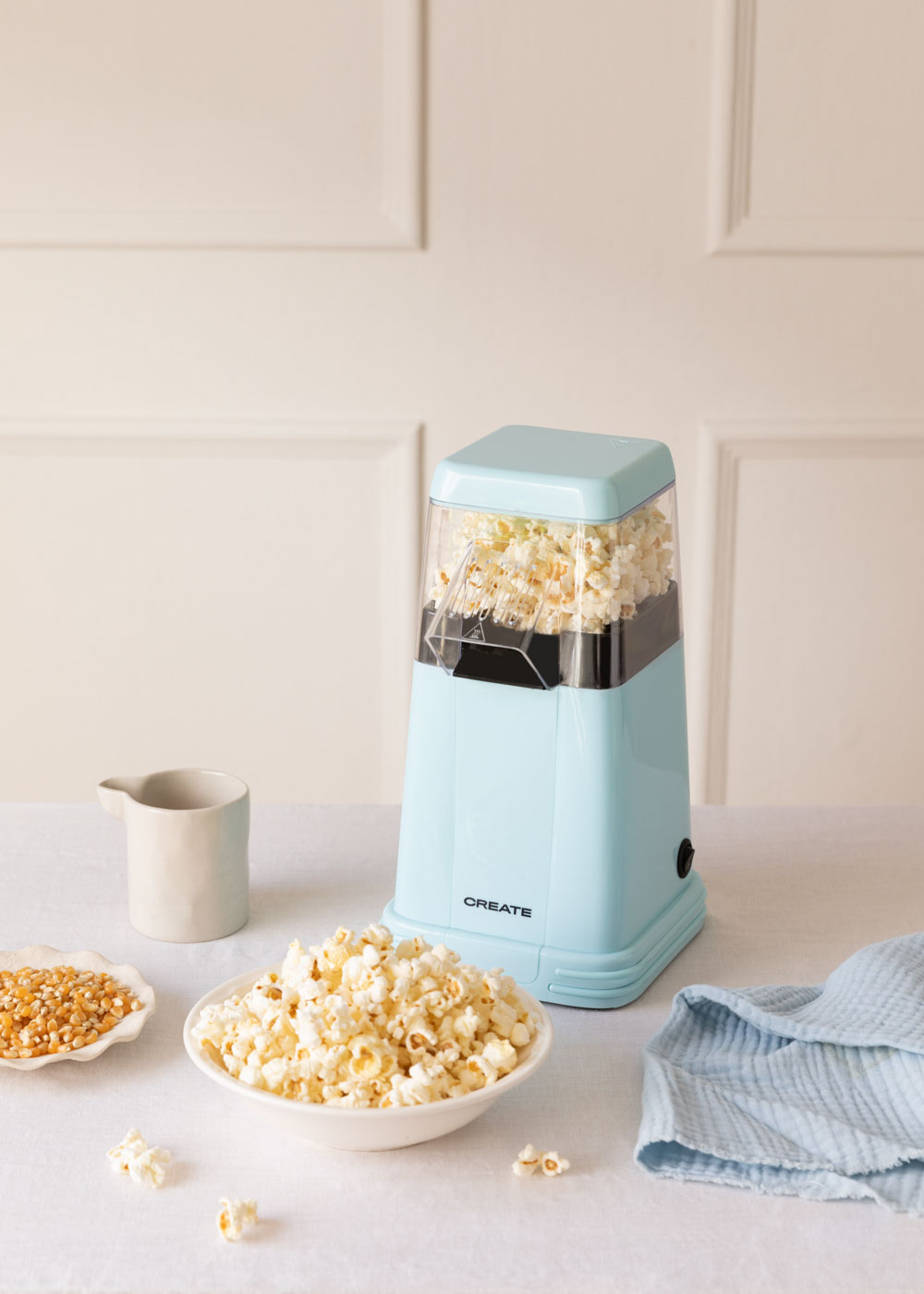 Máquina de palomitas azul claro con palomitas, granos y un tazón de palomitas.